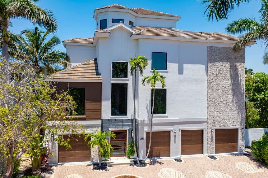 Three-story white stucco home with impact windows and wood garage doors in Bonita Springs